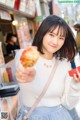 A woman holding up a piece of food in front of a store.