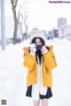 A woman in a yellow jacket is taking a picture in the snow.