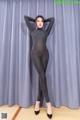 A woman in a black bodysuit posing in front of a curtain.
