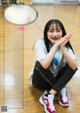 A young woman sitting on a basketball court with her hands clasped together.