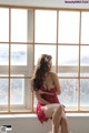 A woman in a red lingerie sitting on a window sill.