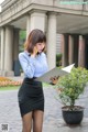 A woman in a blue shirt and black skirt talking on a cell phone.