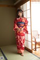 A woman in a red kimono standing in front of a window.