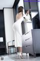 A woman in a white dress standing in front of a dresser.