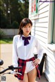 A woman in a white shirt and red plaid skirt posing next to a bike.