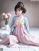 A woman in a pink and blue kimono sitting on a bed.