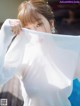 A woman in a white shirt is holding a white scarf over her face.